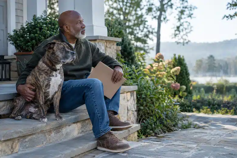 Older man sitting on a porch beside a brindle dog with a closed folder