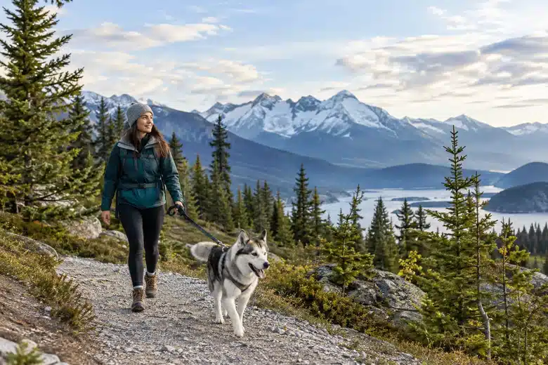 A woman walking a husky mix along a mountain trail