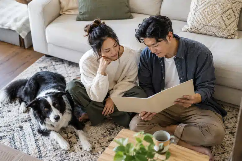 Couple reviewing a plain folder beside a black-and-white dog on a rug